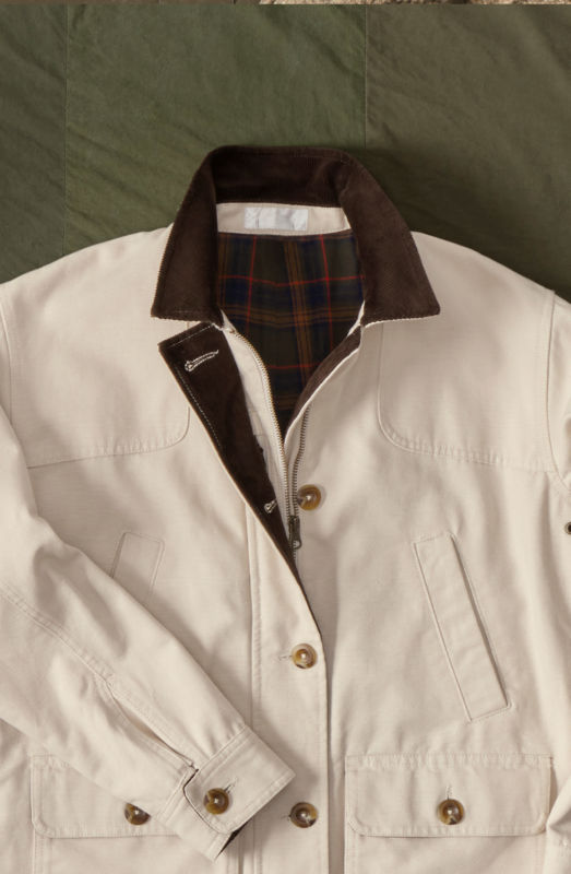 A cream chore coat with plaid lining laid on a green cloth background.