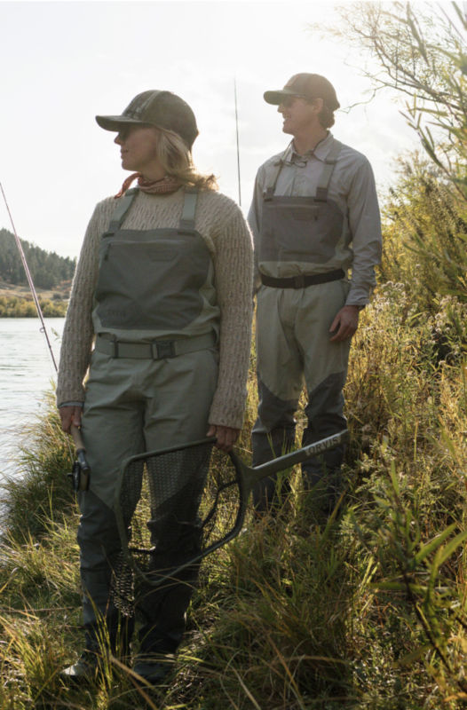 Two anglers walk along a river bank in full wading gear.