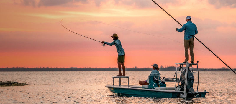 Three people fishing off a boat during a glorious sunrise.
