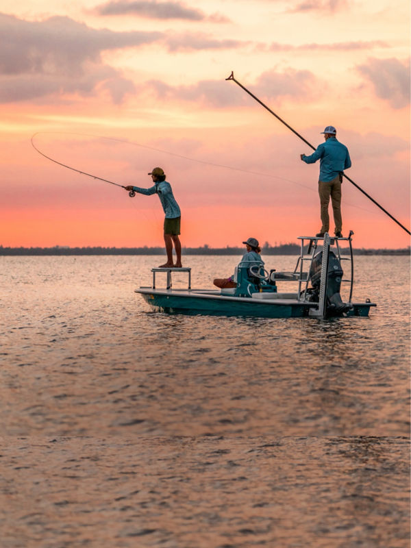 Three people fishing off a boat during a glorious sunrise.
