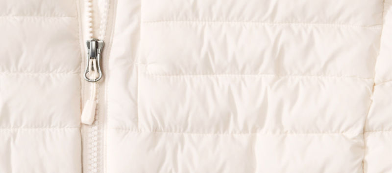 A closeup of the fabric from a cream puffy jacket including the zipper.