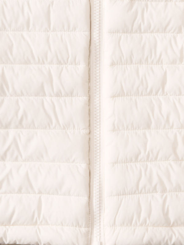A closeup of the fabric from a cream puffy jacket including the zipper.