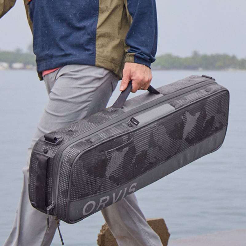 An angler carries a travel pack across a dock.