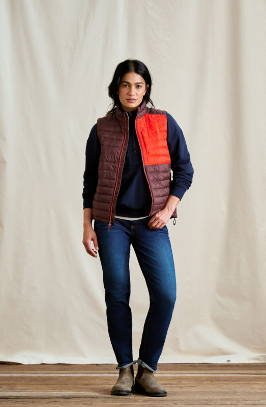 A woman wearing a burgundy vest over a blue sweater and jeans.