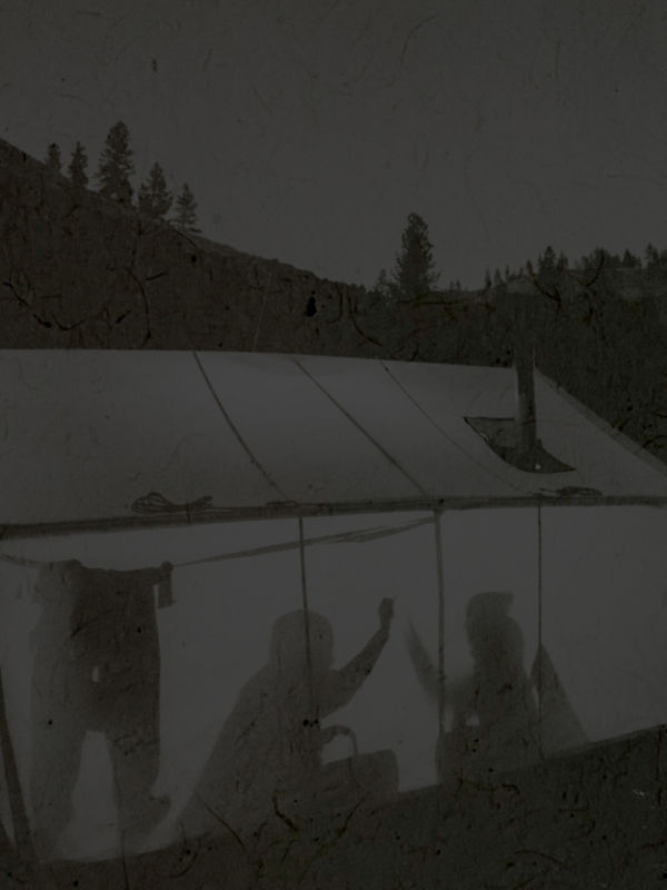 Black and white image of a campsite with two people silhouetted inside their tent.