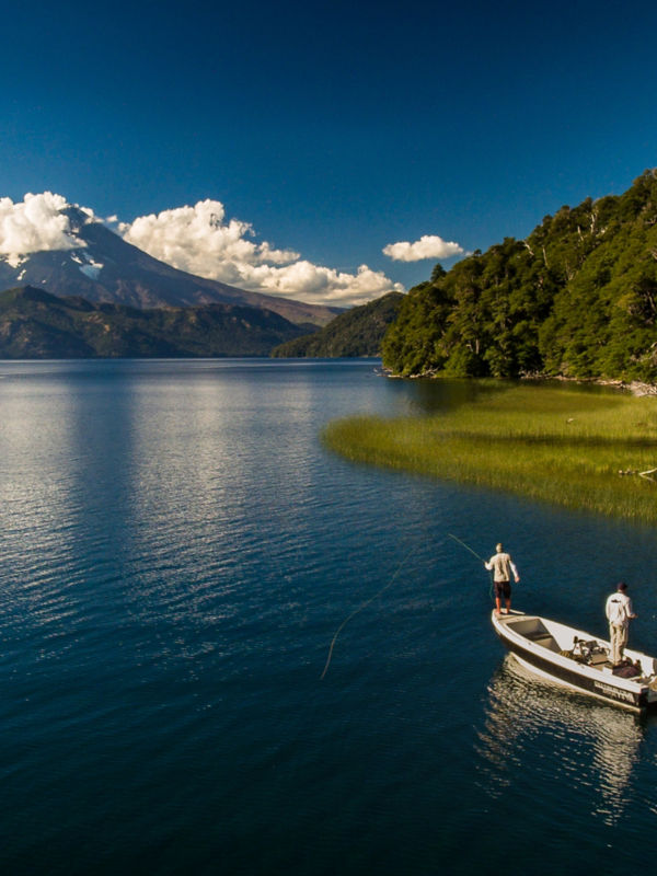 A gorgeous blue water with a small boat plying its way toward the mountains in the distance