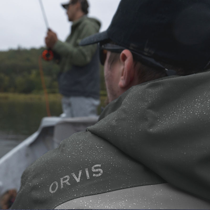 A view of the beaded up shoulder of a rain jacket with an angler beyond.