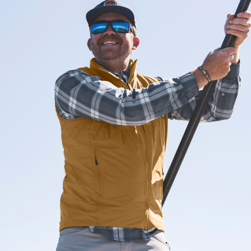 An angler in a gold insulated vests smiles while he poles the boat.