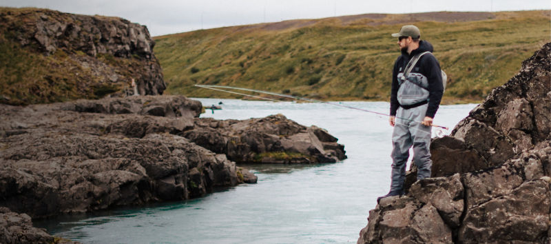 An angler stands on a rock in the middle of a river.