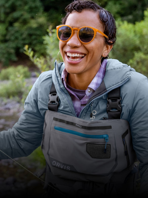 An angler laughing while wearing a pair of waders in a creek.