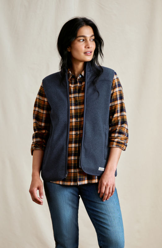 A woman is wearing a navy vest over a brown plaid flannel shirt.