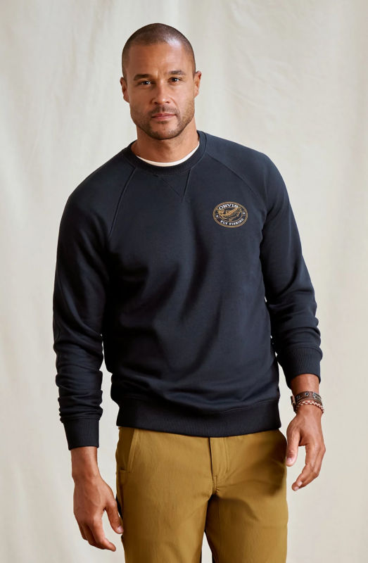 A model wearing a navy sweatshirt with an Orvis logo and tan pants.