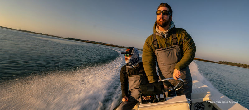 Two people in a small boat speed away from the shore into the rising sun.