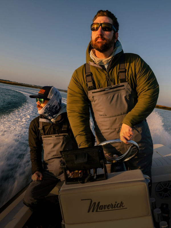 Two people in a small boat speed away from the shore into the rising sun.