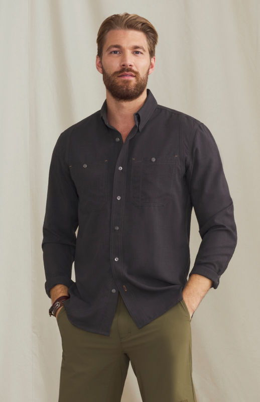 A man wearing a black button-down over olive pants.
