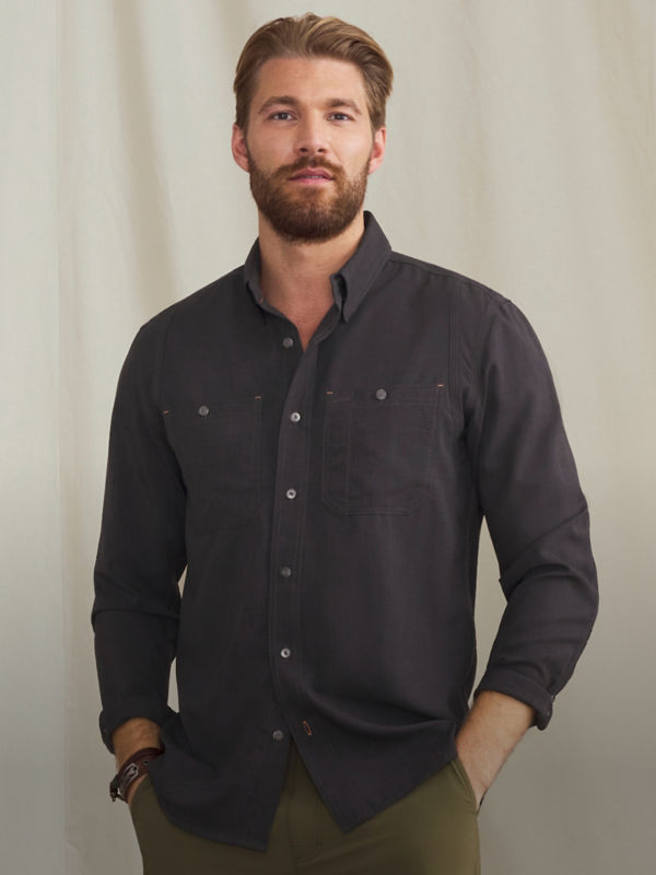 A model wearing a black button-down shirt over olive pants.
