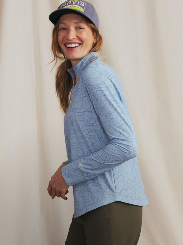 A woman wearing a blue shirt with contour map markings and a navy Orvis ball cap.