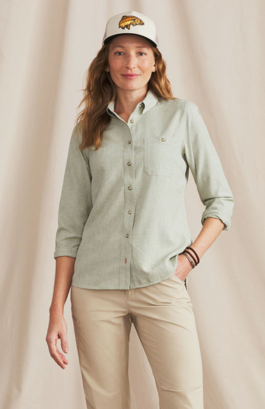 A woman is wearing a light green shirt over cream colored pants and a tan hat.