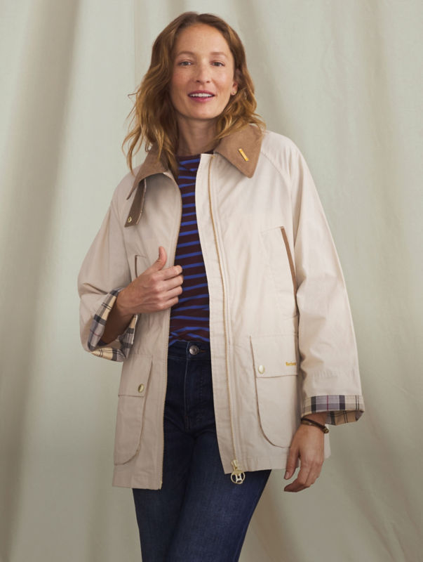 A woman wearing a cream and tan Barbour jacket over a t-shirt and blue jeans.