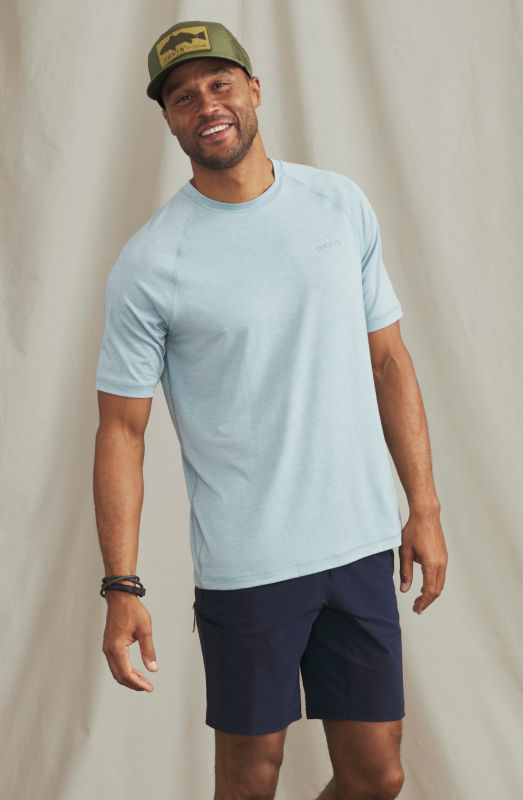A man wearing a light blue sun protection shirt with an olive Orvis ball cap.