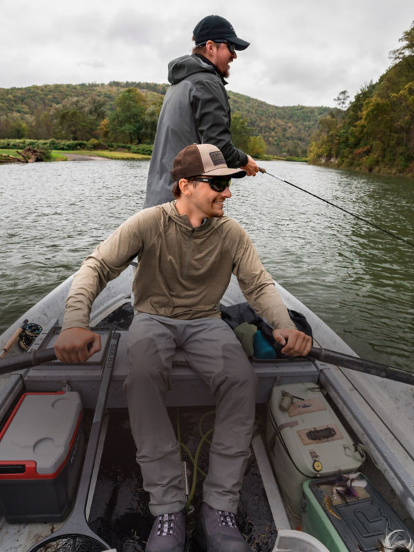 A smiling angler rows a boat while another stands behind him with a fly rod in hand.