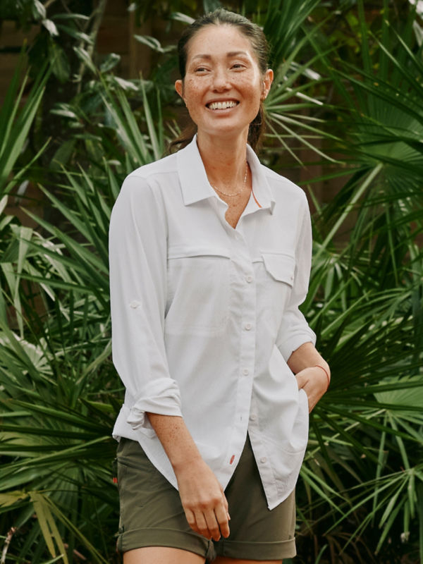 A model wearing a white shirt over olive shorts with plants in the background.