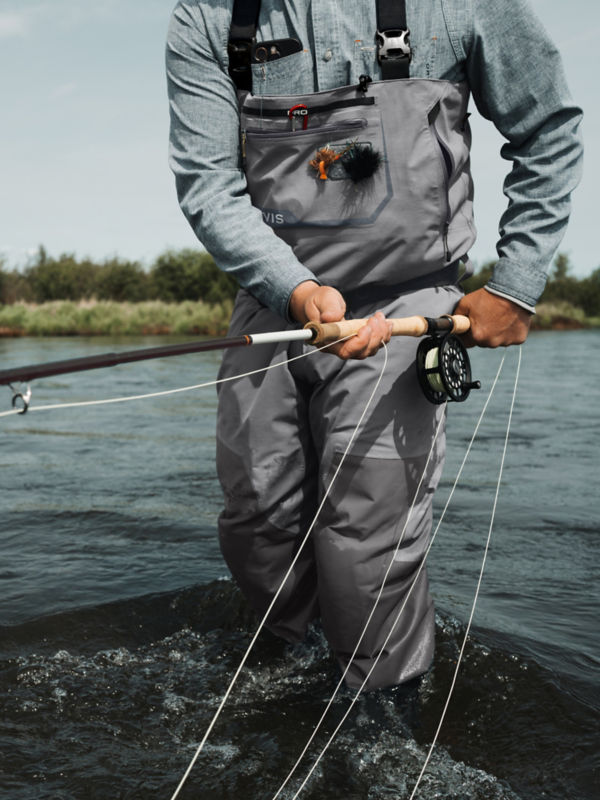 An angler in waders with a fly rod down by his hip.