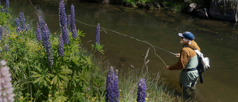 A man holding a fishing rod wearing a tan jacket and waders.