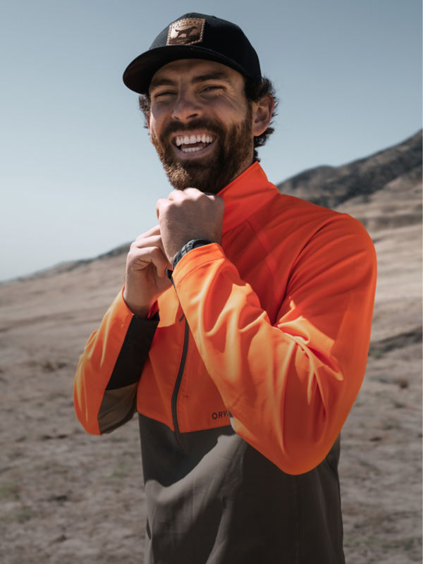 A smiling hunter zips up his blaze orange and khaki quarter-zip.