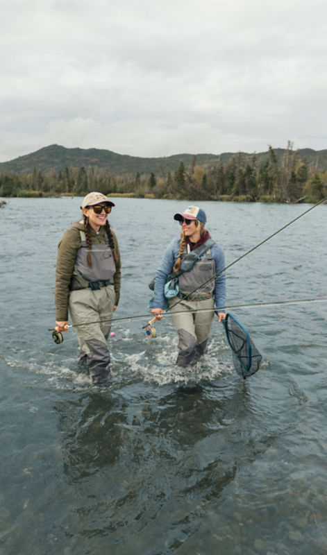 Two anglers wade through a river with their fly rods in hand.