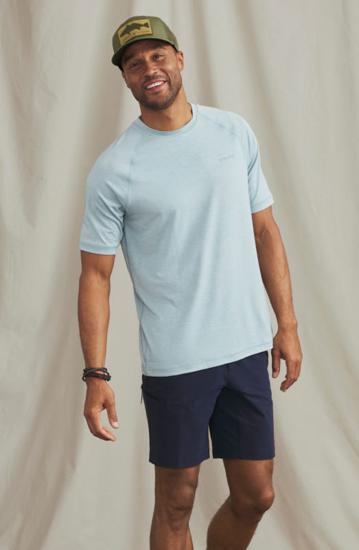 A model wearing a light blue sun protection t-shirt over dark blue shorts.