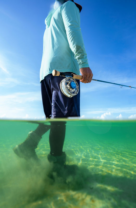 An angler wearing a light blue sun protection hoodie over dark blue shorts walking the Flats.