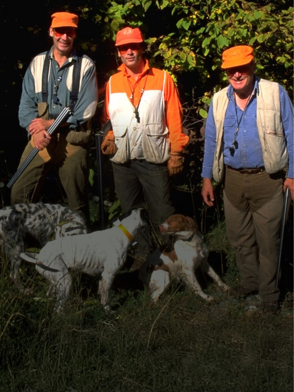 Three men and their dogs in hunting clothes and eye protection.