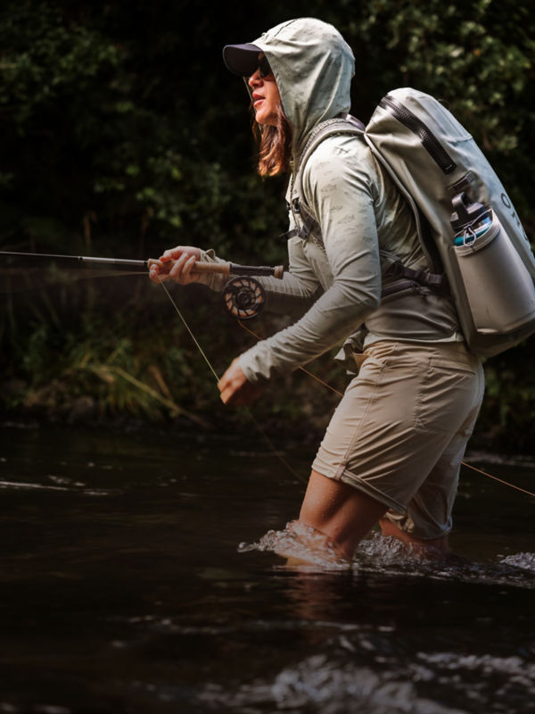 An angler in sun protective clothing fishes in shorts from mid-river.