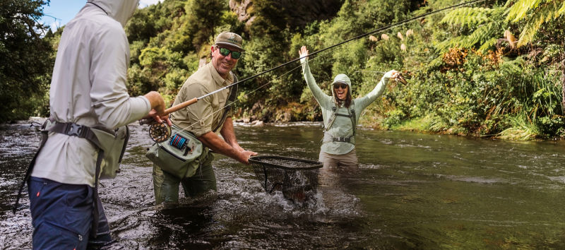 A group of people fishing together in a river  excited about a fish in a net.