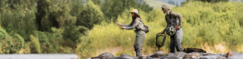 Two anglers in waders fishing a rocky river in New Zealand.