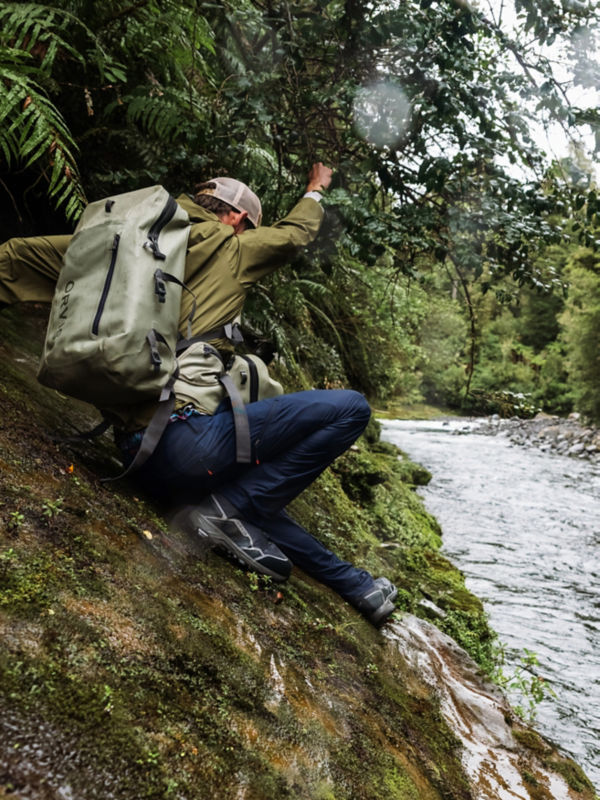 A man carrying a waterproof backpack slides down a rocky river to a river.