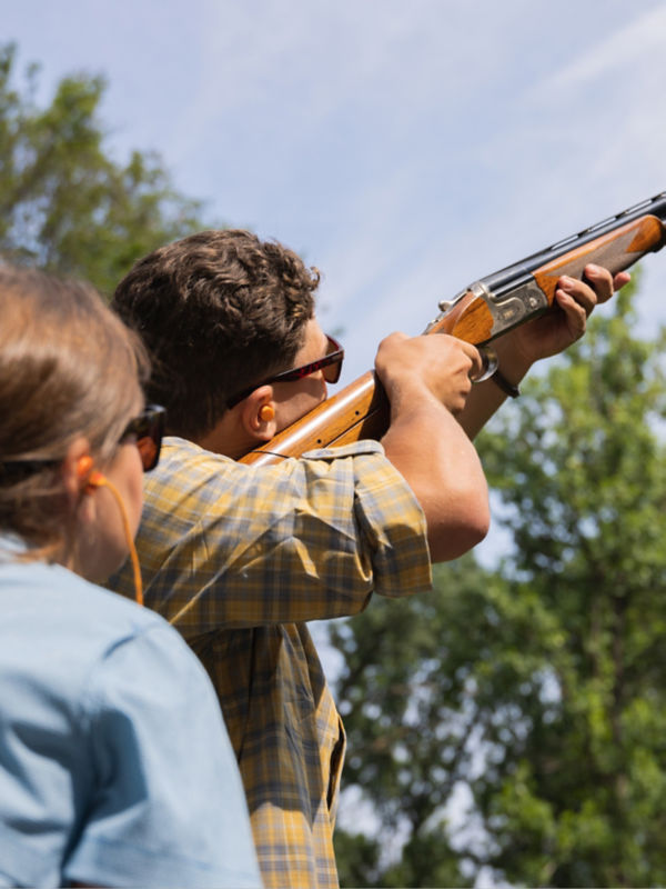 An instructor watches over a student's shoulder as he aims.