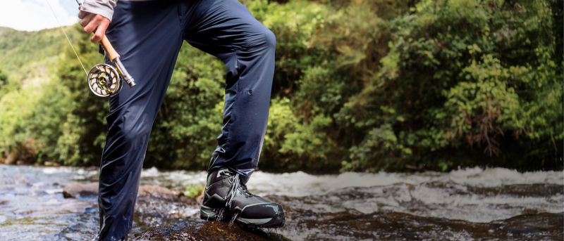 The wet pants of a wading angler as they step out of the river onto a rock.