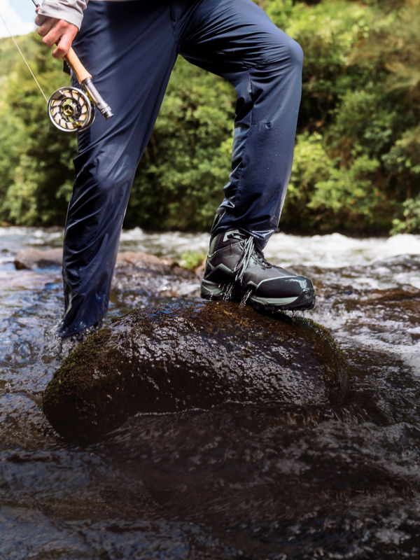 The wet pants of a wading angler as they step out of the river onto a rock.