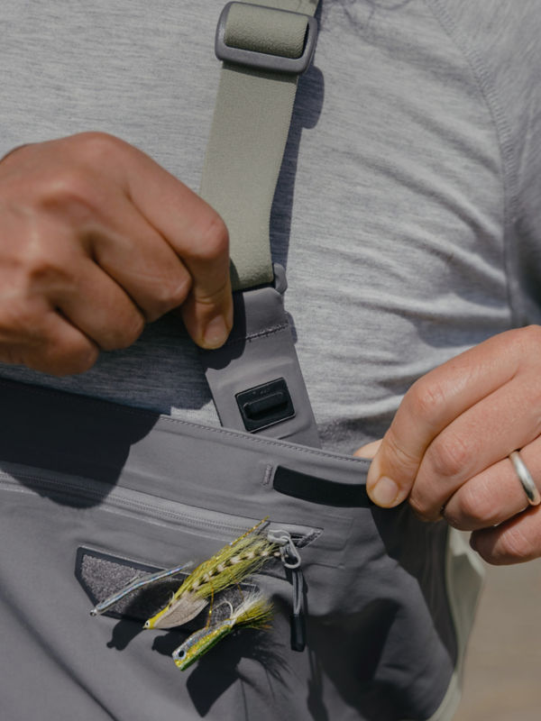 An angler snaps his shoulder strap to the body of his waders.