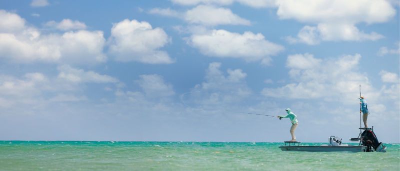 An angler fly fishing from a small motorboat in tropical waters.