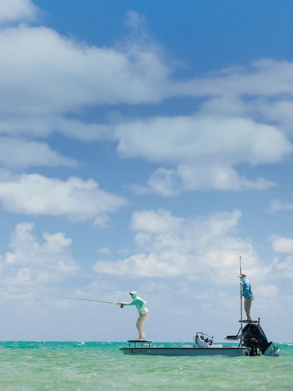 An angler fly fishing from a small motorboat in tropical waters.