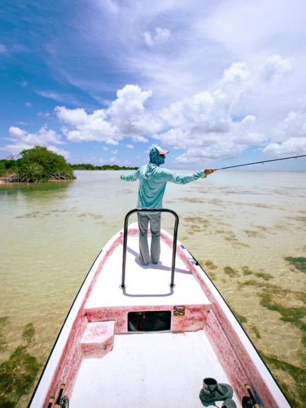 An angler casting from a shallow water boat under a dramatic blue and cloudy sky.
