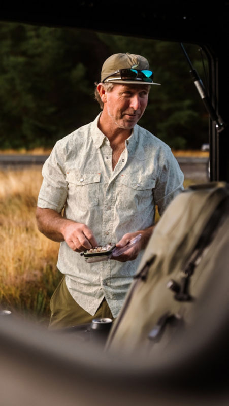 An angler in a light button-down shirt picks through his fly box.