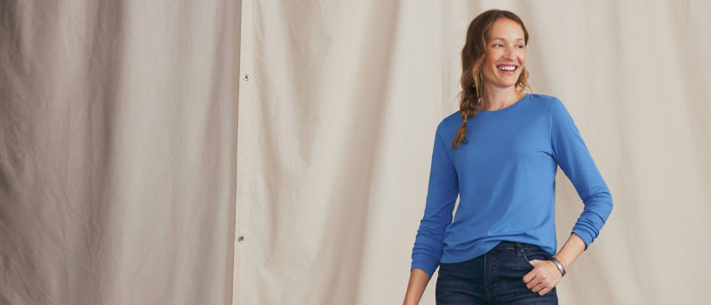 A model wearing a royal blue long sleeved t shirt over dark wash jeans with her left thumb in pocket.