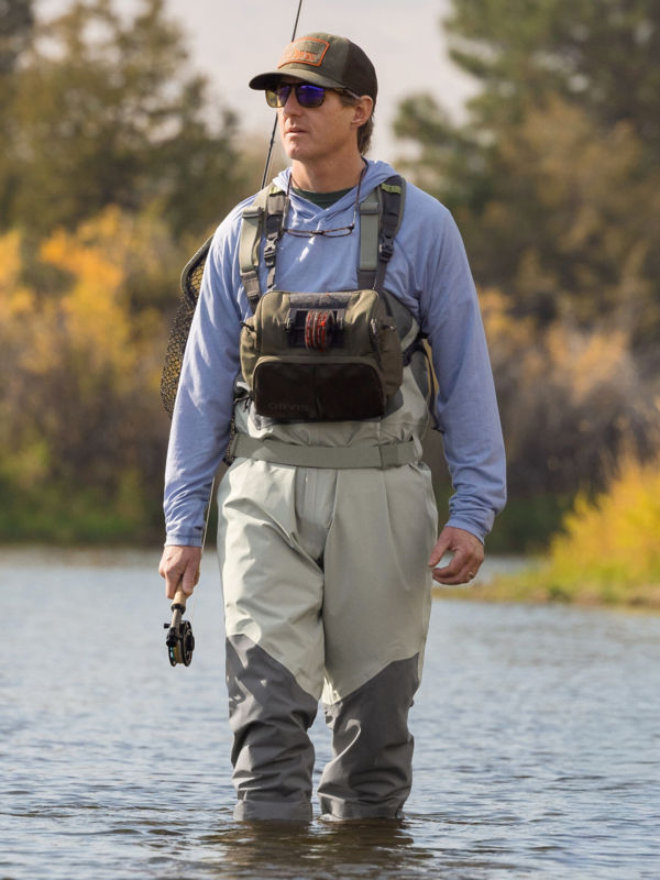 An angler walks calf-deep through river water.