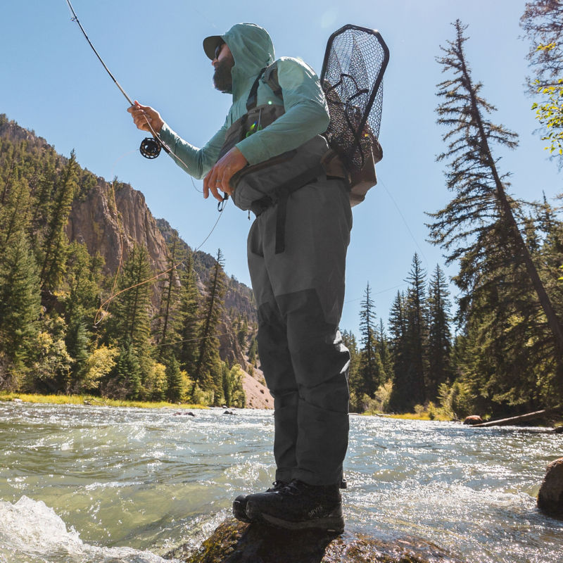 A man in waders casts from a rock stream-side.