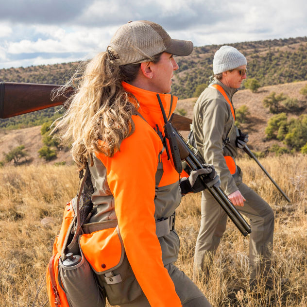 Two hunters climb a hill of dry grass.