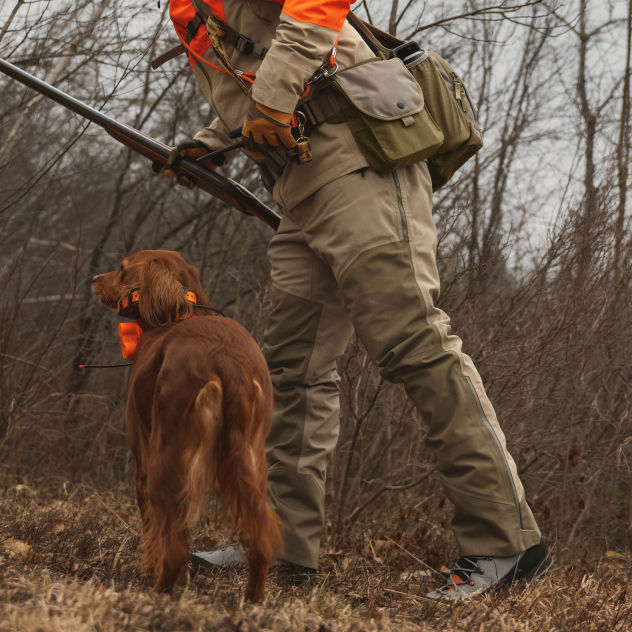 A hunter leans over his golden red dog in the barren brush.